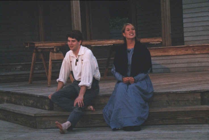 Two characters seated together on stage