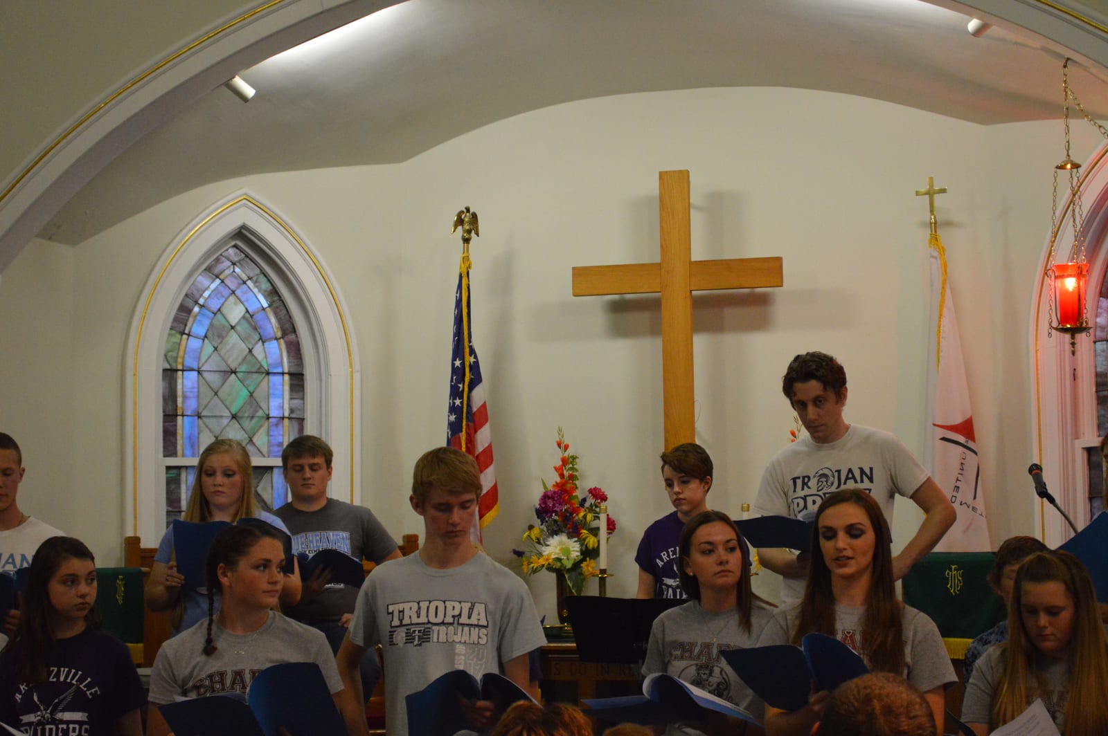The cast singing before the cross and flags, wearing Triopia, Chapin, and Arenzville school shirts