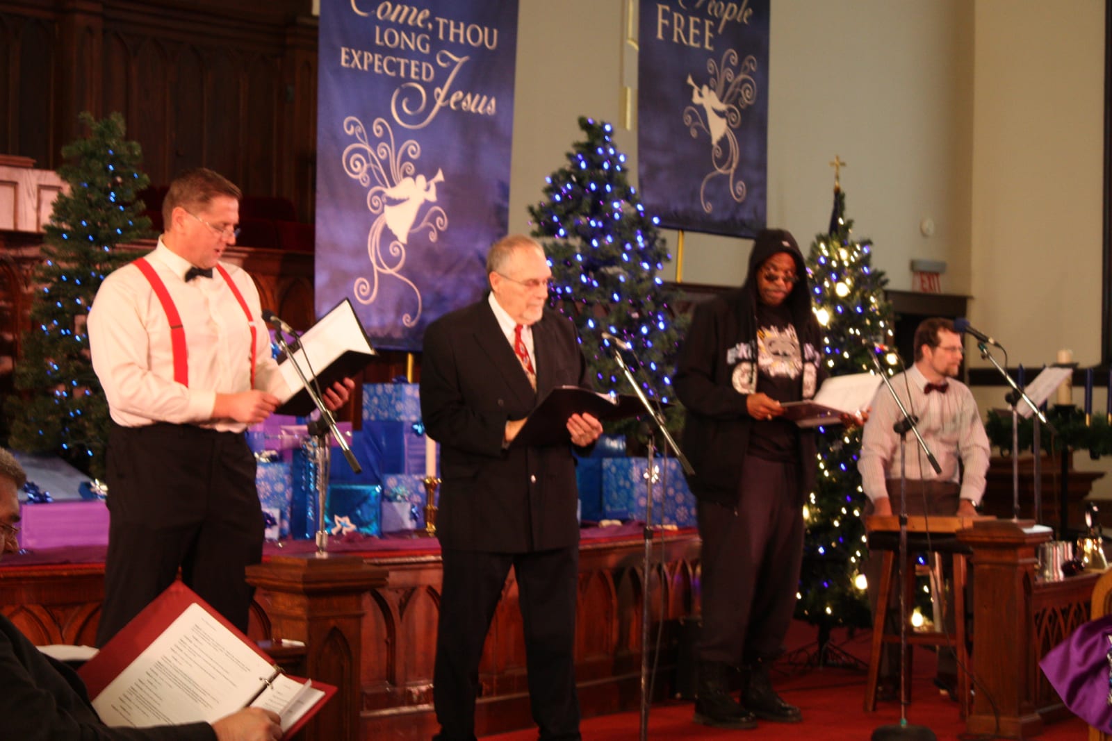 Actors step to the microphones with scripts, Christmas trees behind