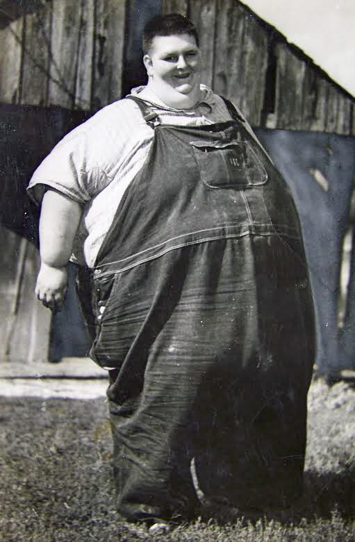 Robert Earl Hughes standing in overalls outside a barn