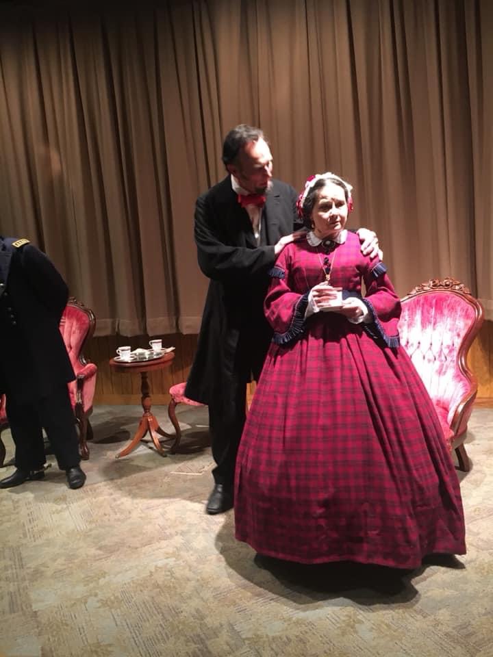 Mary Todd Lincoln seated with a teacup, listening to Lincoln